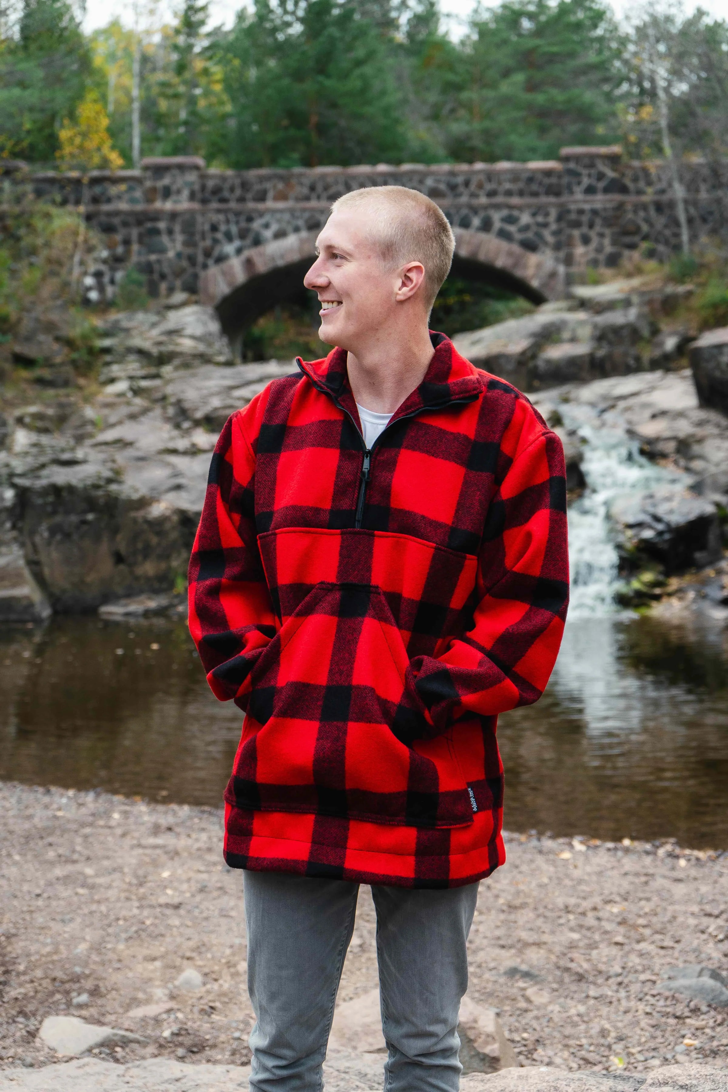 A man wearing a Duluth Pack Red Buffalo Plaid Blanket Shirt looking to the side and standing in front of a waterfall. 