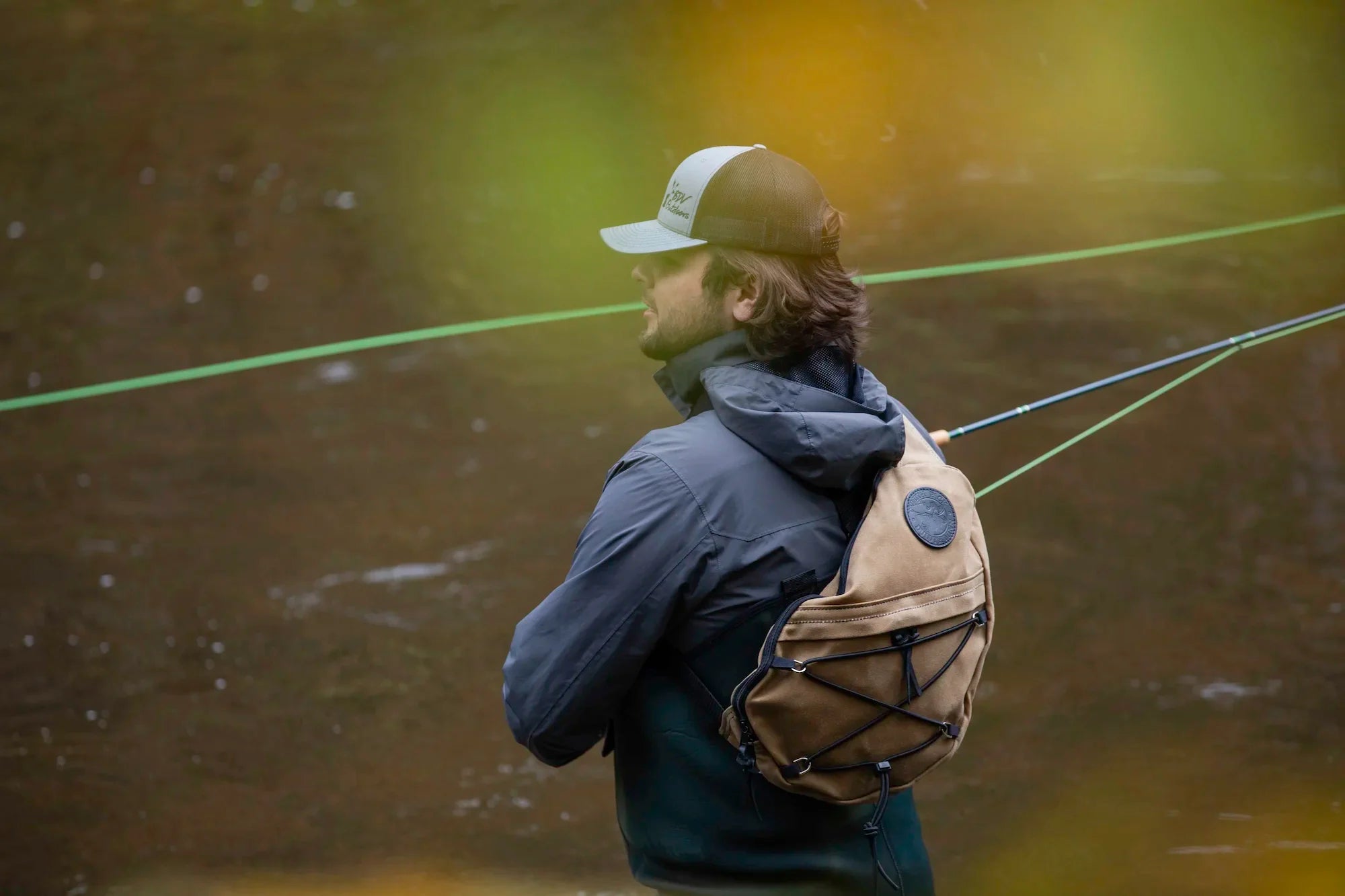 A man fly fishing on the Brule River with a Waxed Khaki Sling Pack by Duluth Pack. 