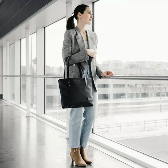 Superior Series Leather Lakewalk Tote in black leather with riveted handles, carried by a woman wearing a gray blazer and jeans in a modern indoor setting.