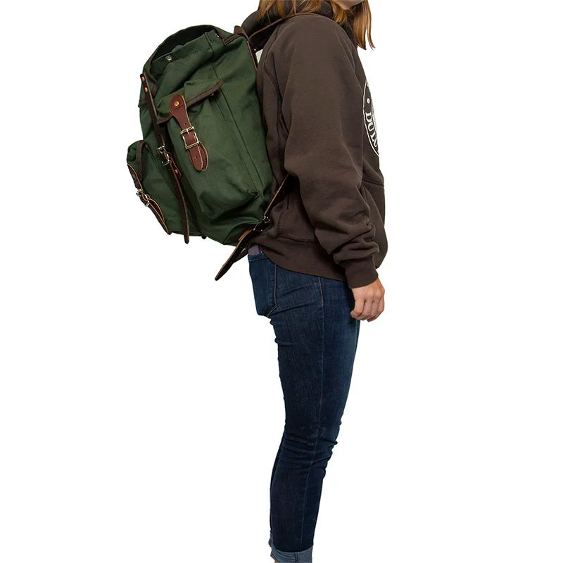 Wanderer backpack in Olive Drab with hand-cut leather reinforcements worn by a person, showcasing rugged handmade canvas gear for outdoor adventures.