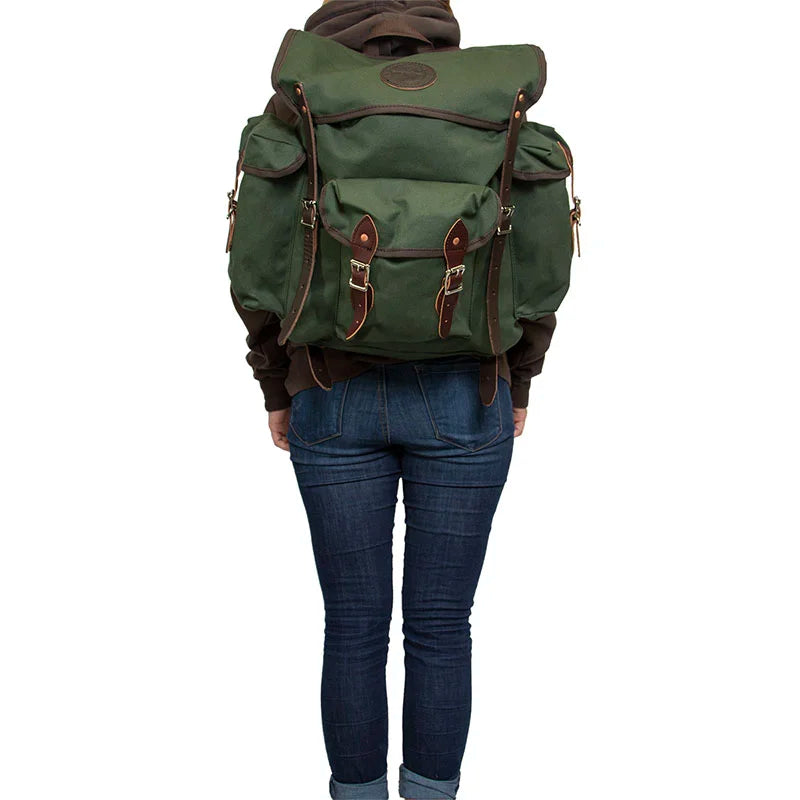 Wanderer backpack in Olive Drab with hand-cut leather reinforcements, durable canvas for rugged outdoor use, worn by a person dressed for adventure.