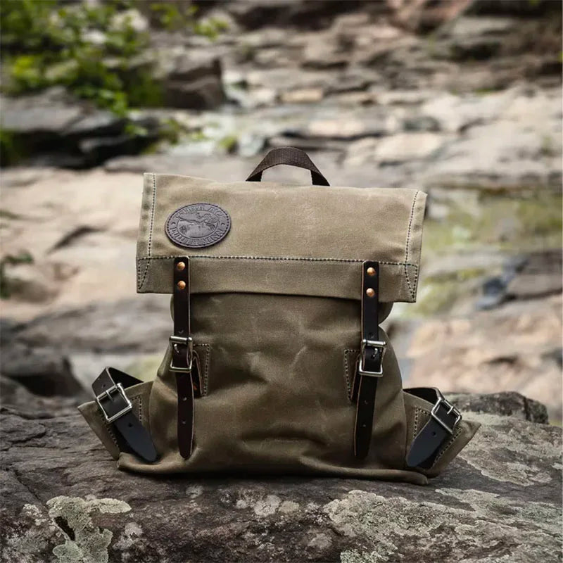 Scout Pack in Waxed Khaki canvas with leather straps, set on a natural rocky outdoor background showcasing its durable, handmade craftsmanship for rugged use.