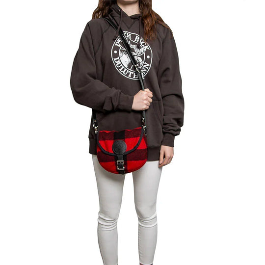 Classic Wool Small Shell Purse in red and black wool plaid, worn crossbody by a person in casual outdoor attire, highlighting its rugged handmade quality for everyday use.