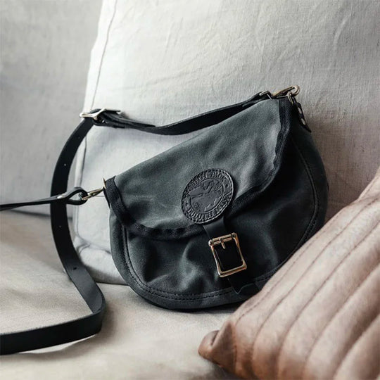 Small Shell Purse in black rugged 15-ounce canvas with adjustable premium leather shoulder strap, shown resting on a cozy fabric surface by Duluth Pack.