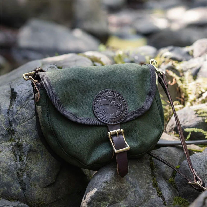 Small Shell Purse in olive drab with premium leather strap, crafted from rugged canvas, resting on outdoor rocks showcasing durable heritage design by Duluth Pack.