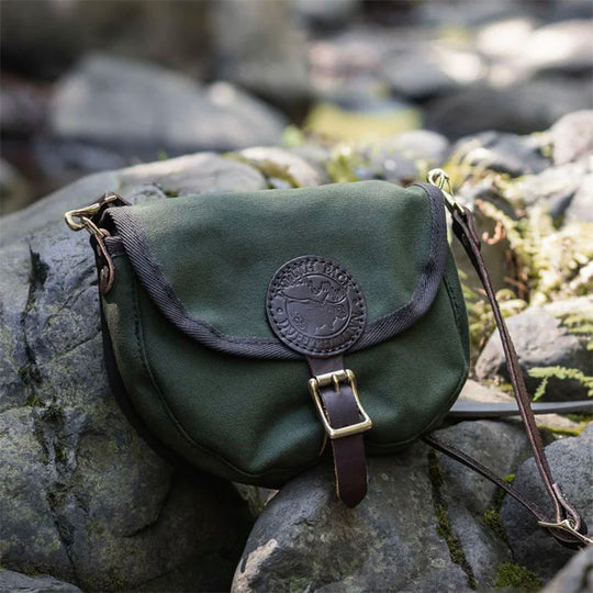 Small Shell Purse in olive drab with premium leather strap, crafted from rugged canvas, resting on outdoor rocks showcasing durable heritage design by Duluth Pack.