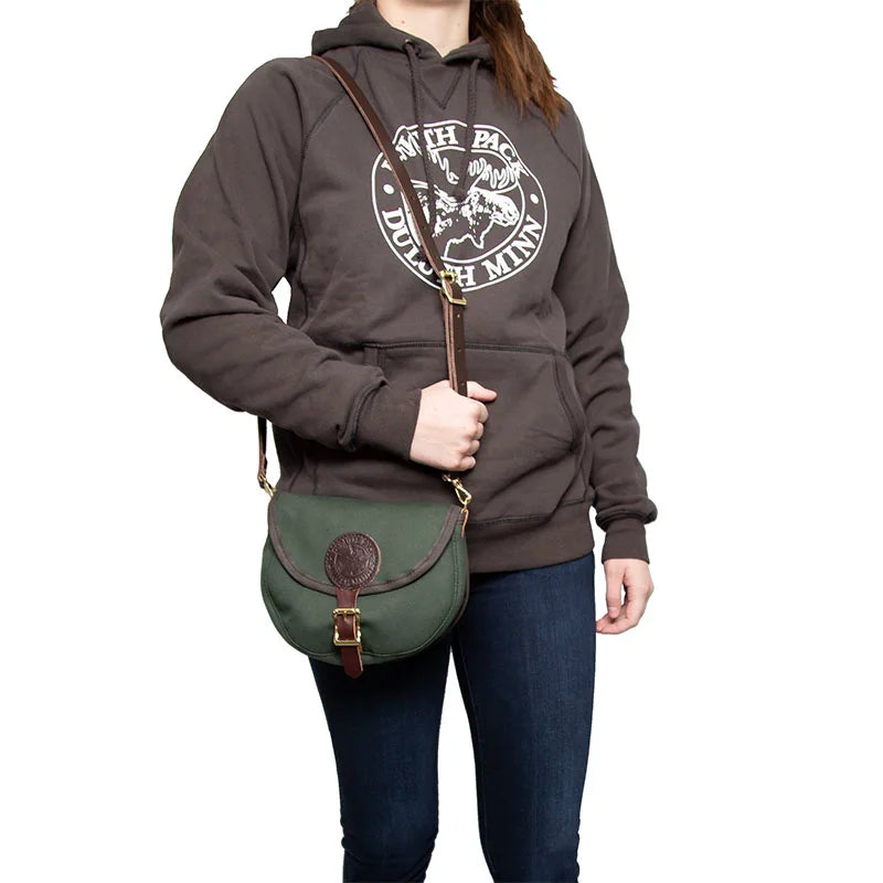 Small Shell Purse in Olive Drab with adjustable leather strap worn crossbody by person in casual dark hoodie, showcasing rugged handmade canvas and leather outdoor style.