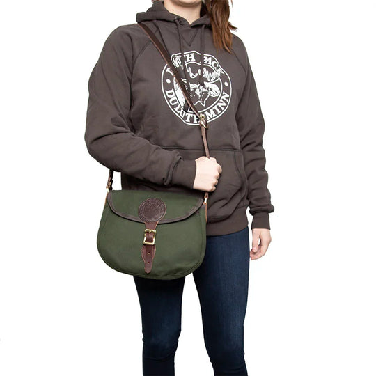 Medium Shell Purse in Olive Drab with leather accents by Duluth Pack, worn crossbody by a person in casual outdoor clothing, showcasing heritage craftsmanship.