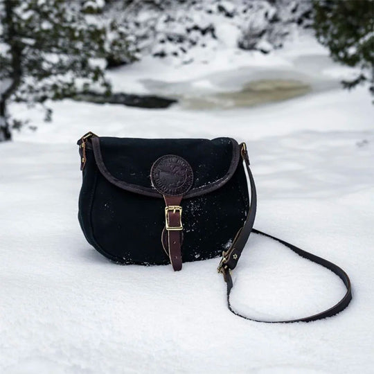 Medium Shell Purse in black with antique brass hardware, handcrafted from durable canvas and leather, set on a snowy outdoor background highlighting rugged performance.