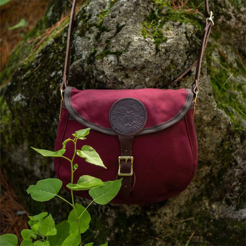 Medium Shell Purse in Burgundy with leather accents from Duluth Pack, displayed outdoors against a mossy rock background highlighting durable canvas craftsmanship.