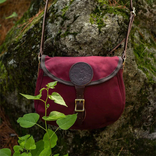 Medium Shell Purse in Burgundy with leather accents from Duluth Pack, displayed outdoors against a mossy rock background highlighting durable canvas craftsmanship.
