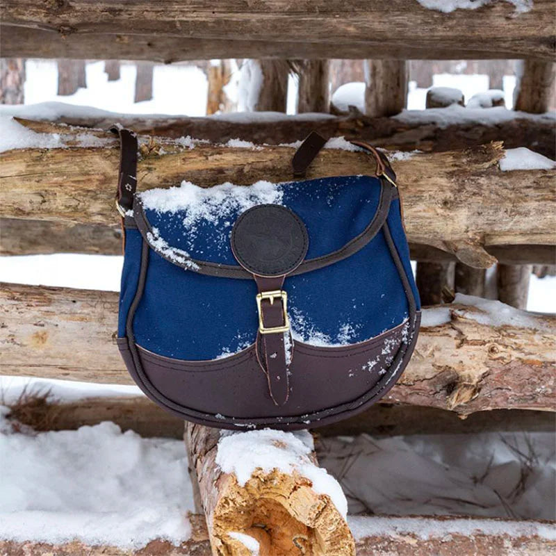 Deluxe Medium Shell Purse in navy with brown leather accents from Duluth Pack, resting on snow-covered logs in a rustic outdoor setting.