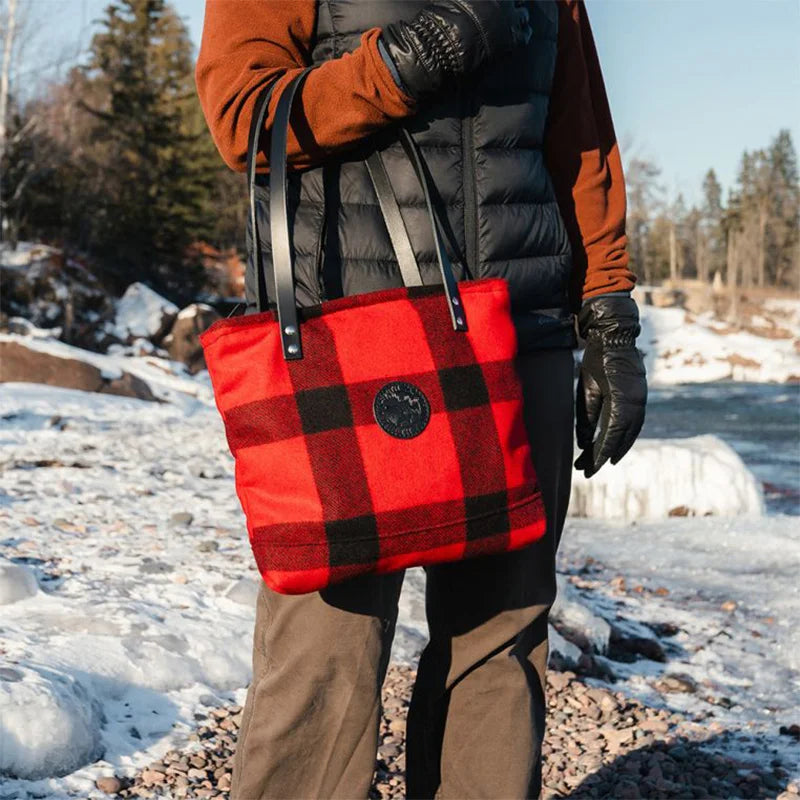 Classic Wool Lakewalk Tote in red and black wool plaid with riveted leather straps, carried outdoors in a snowy lakeside setting.