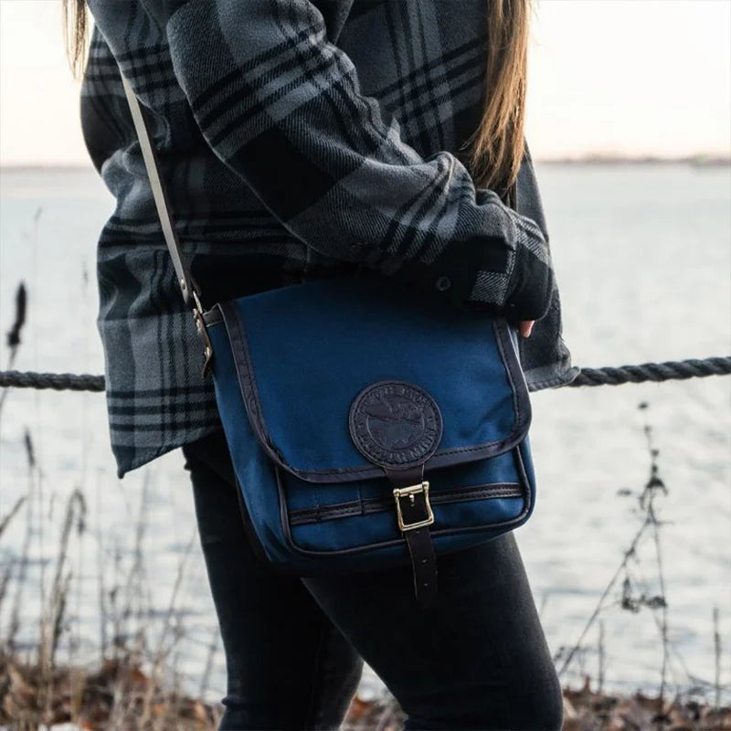 Mini Haversack Purse in navy canvas with leather accents, worn outdoors near a waterfront, showcasing durable craftsmanship for everyday and travel use.