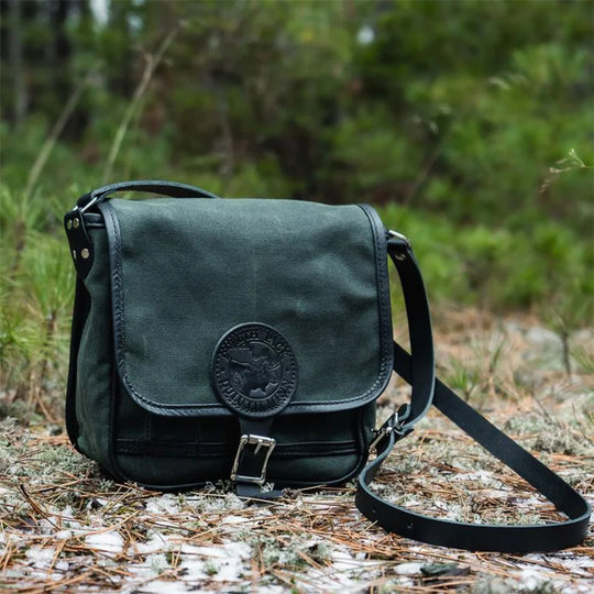 Mini Haversack Purse in Waxed Olive Drab canvas with leather accents, outdoors on a forest floor showcasing rugged outdoor style and durability.