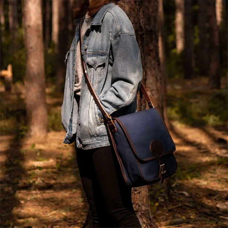 Haversack in rugged navy 15-ounce canvas with leather accents and antique brass hardware, worn outdoors in a forest setting by Duluth Pack