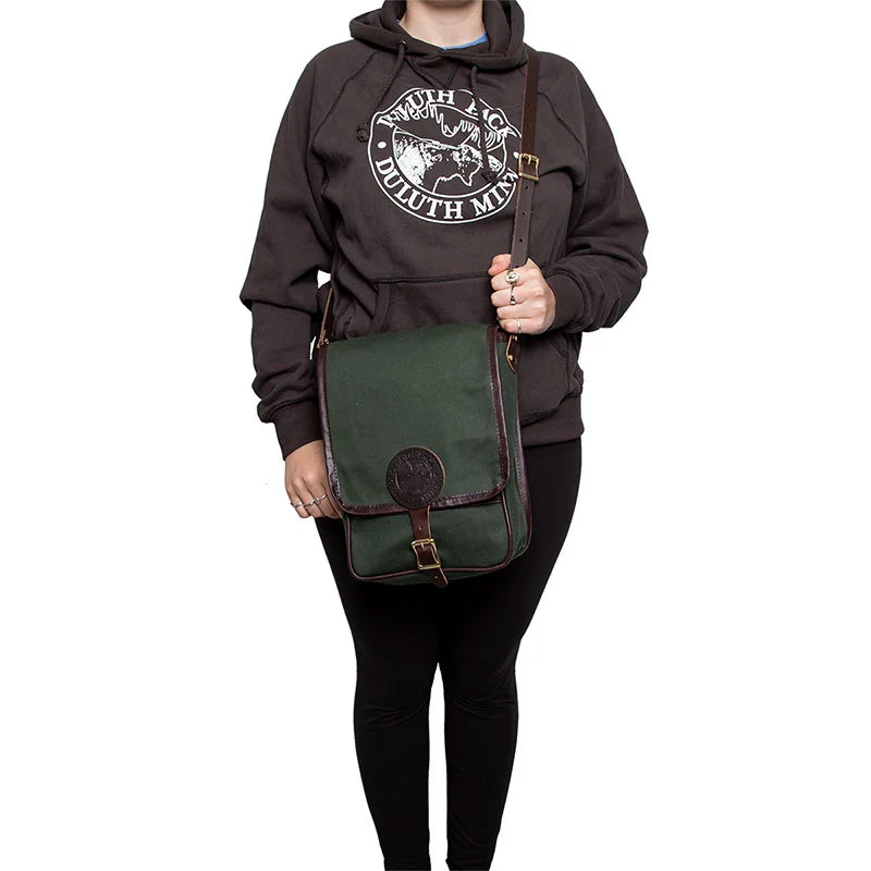 Haversack with rugged 15-ounce canvas and premium leather strap worn over the shoulder by a person in casual outdoor attire, emphasizing durable outdoor gear.