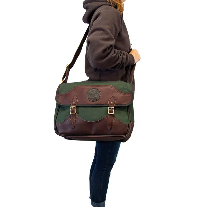 Deluxe Book Bag in Olive Drab with handcrafted leather trim, worn by a person outdoors, showcasing rugged canvas durability from Duluth Pack heritage craftsmanship.