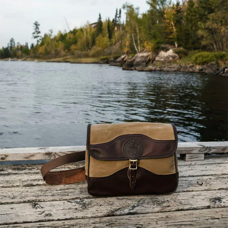 Field Satchel in rugged 15-ounce canvas with premium leather accents, resting on a weathered dock by a serene lake, highlighting durable outdoor craftsmanship.