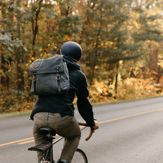Ranger Pack in Waxed Grey canvas with leather straps worn by a cyclist riding along a forest road in autumn, highlighting tough outdoor durability.