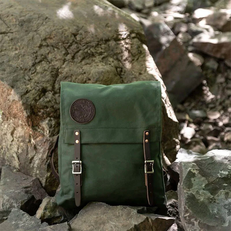 Ranger Pack in Olive Drab with premium leather flap straps resting on rugged rocks, showcasing durable canvas craftsmanship for outdoor adventures.