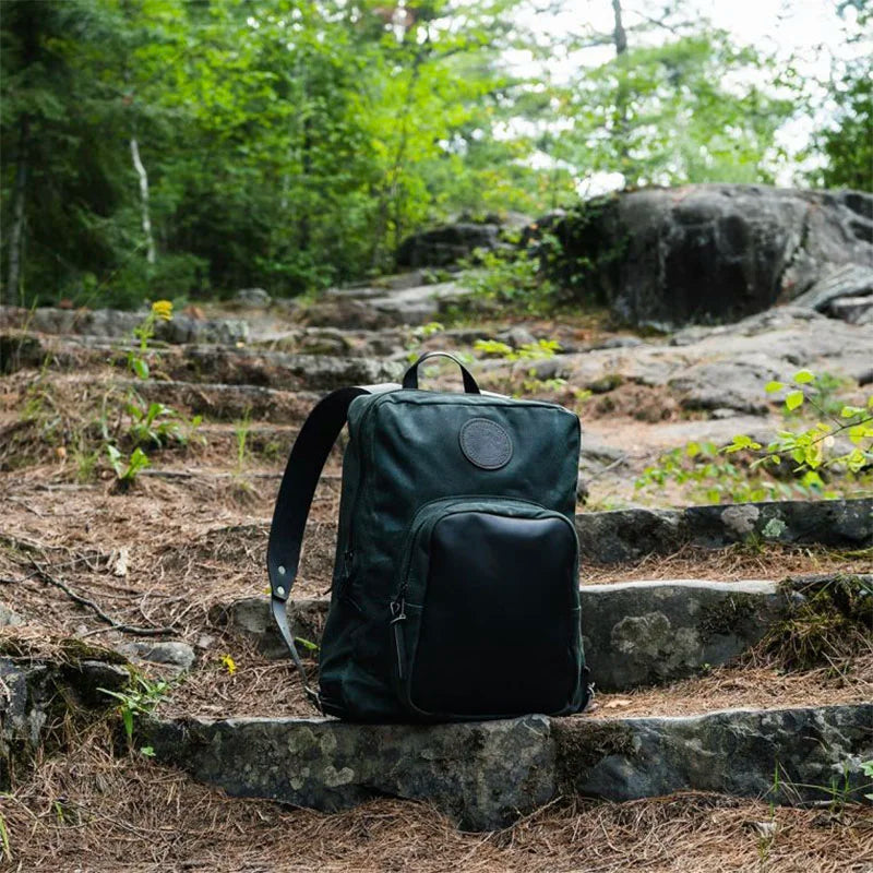 Deluxe Laptop Backpack in Mossy Oak Bottomland Camo by Duluth Pack, made with rugged canvas and leather, pictured outdoors on stone steps in a forest setting.