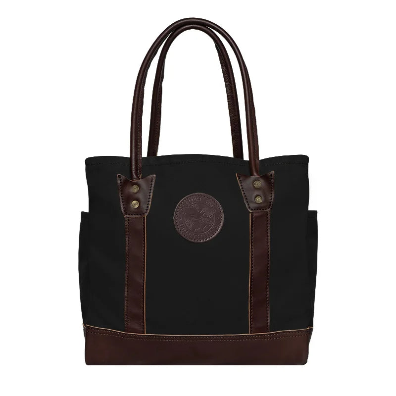 Highlander Tote in black with brown leather accents, handmade by Duluth Pack, designed for durable outdoor use and versatile everyday carrying.