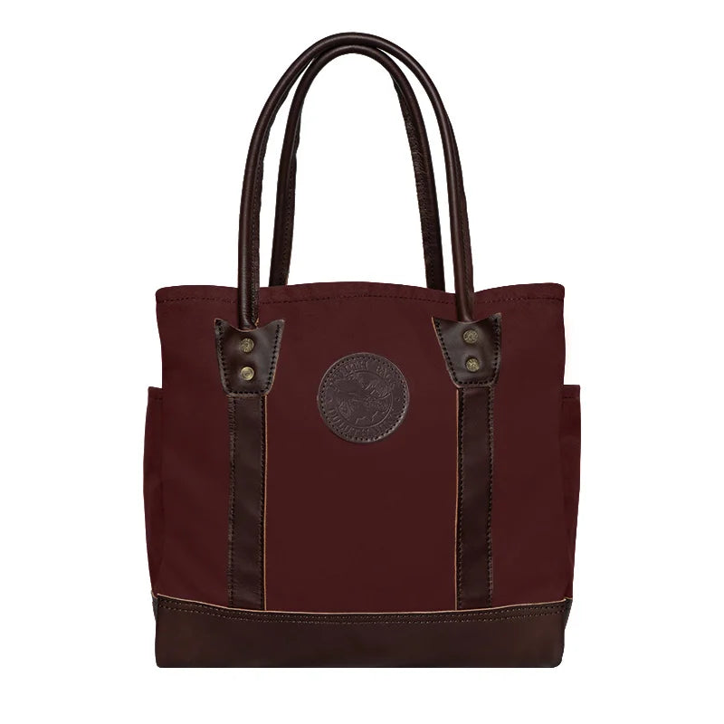 Highlander Tote in burgundy with leather accents featuring durable canvas construction, designed by Duluth Pack for versatile everyday use and rugged outdoor settings.