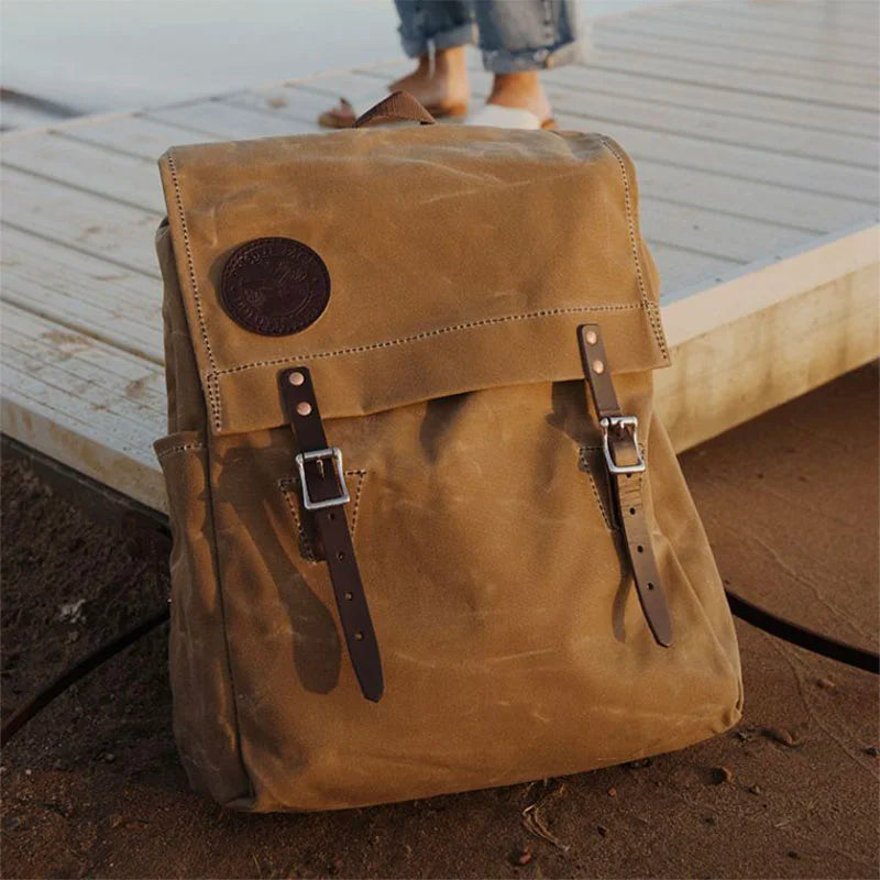 Laptop Scoutmaster in waxed khaki canvas with leather straps, handcrafted for durability and rugged outdoor use by Duluth Pack near a dock setting.