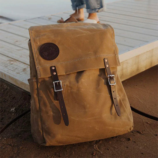 Laptop Scoutmaster in waxed khaki canvas with leather straps, handcrafted for durability and rugged outdoor use by Duluth Pack near a dock setting.