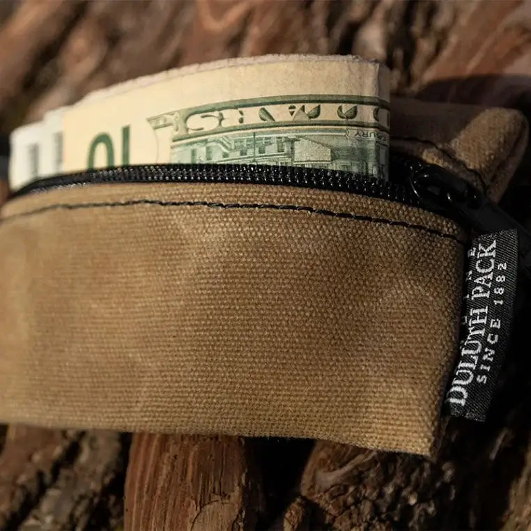 A Mini Gear Stash Bag in Waxed Khaki With Some Money Sticking Out On A Log Background