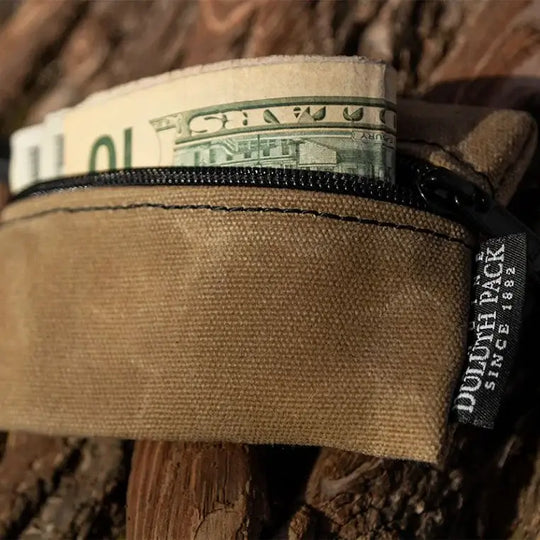 A Mini Gear Stash Bag in Waxed Khaki With Some Money Sticking Out On A Log Background