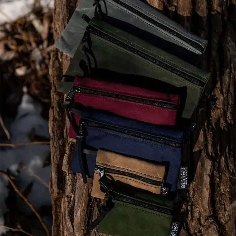 A Size Comparison Of All 3 Sizes Of The Gear Stash Bag (2 of each size in various colors) resting on a log.