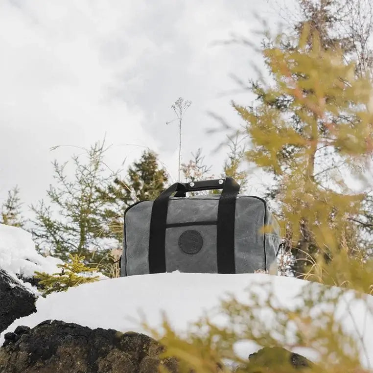 Small Safari Duffel In Waxed Grey Sitting In The Snow In The Forrest