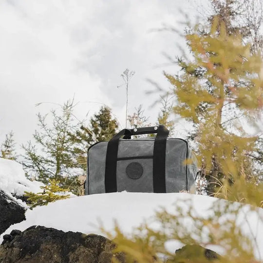 Small Safari Duffel In Waxed Grey Sitting In The Snow In The Forrest