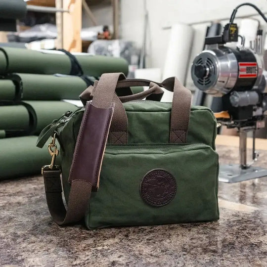 Range Bag Resting On A Table With Roles Of Canvas And A Canvas  Cutting Saw Above It