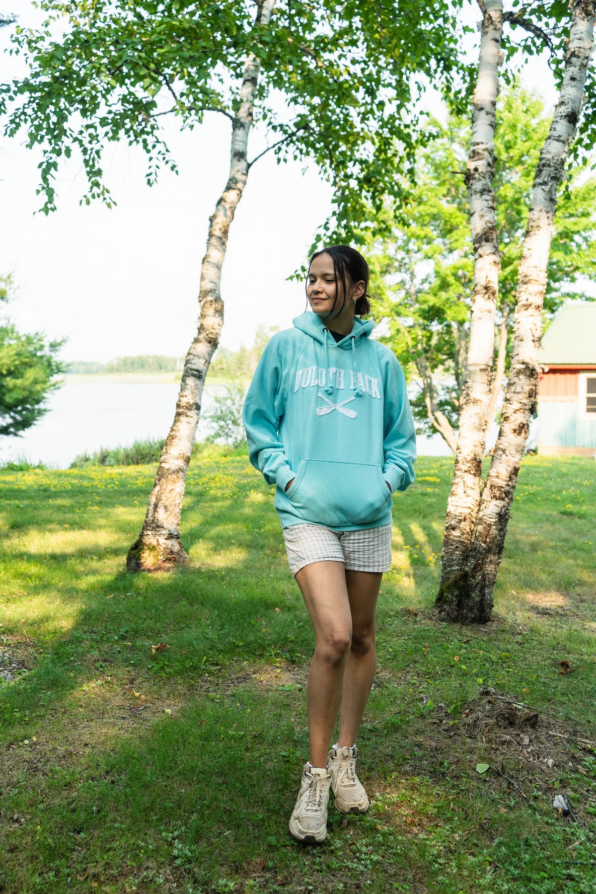 A girl wearing a Duluth Pack Sweatshirt that is teal blue with trees in the background