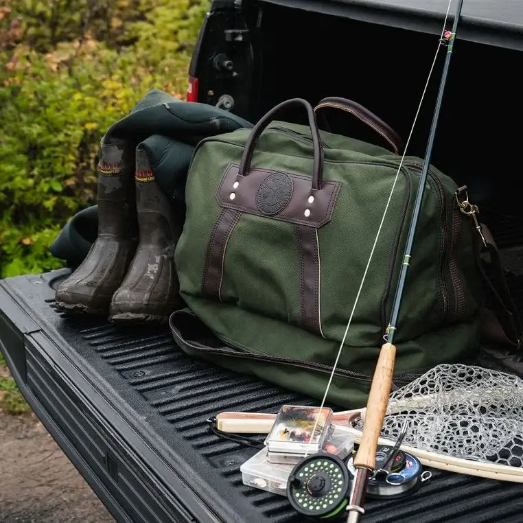 The Boot Duffel In Olive Drab Green Sits On The Tailgate Of A Truck With A Pair Of Waders Next To It On One Side And Fly Fishing Gear Next To It On The Other Side