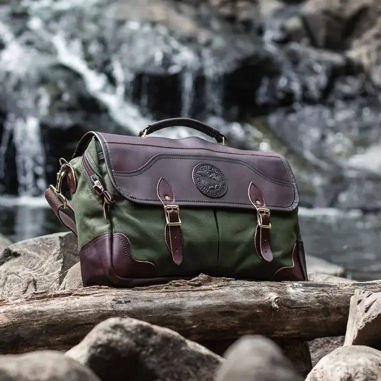 The Entrepreneur Briefcase In Olive Drab Green Sitting In The Rocks Near A Fallen Tree With A Waterfall Behind It