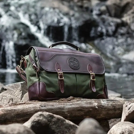 The Entrepreneur Briefcase In Olive Drab Green Sitting In The Rocks Near A Fallen Tree With A Waterfall Behind It