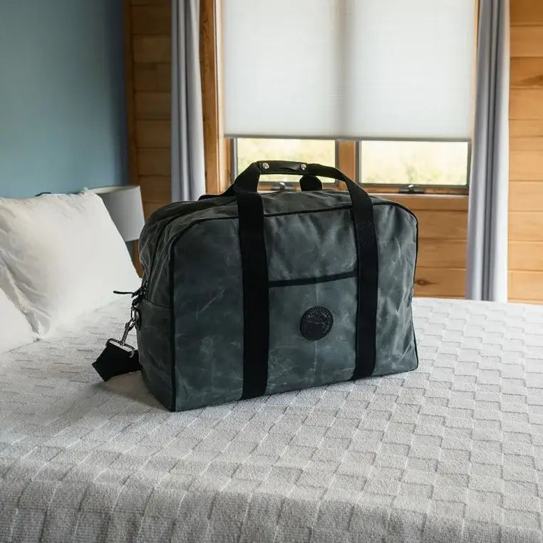 Medium Safari Duffel In Waxed Grey On A Bed In A Hotel