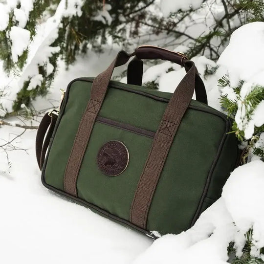 Safari Briefcase In Olive Drab Green Sitting In The Snow Under Pine Trees
