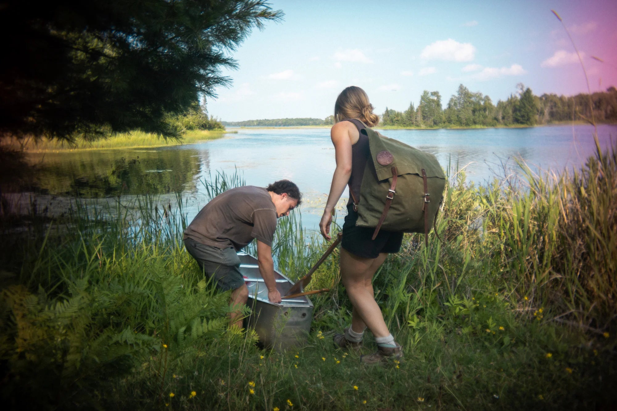 Two people in the Boundary Waters Canoe Area putting their canoe into the water wearing a Duluth Pack Canoe Pack. 