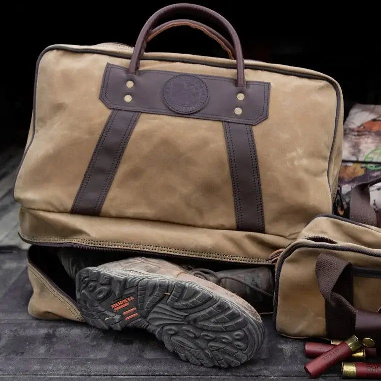 The Boot Duffel In Waxed Khaki Sits On The Tailgate Of A Truck With A Pair Of Boots Coming Out Of The Weather Proof Boot Pocket