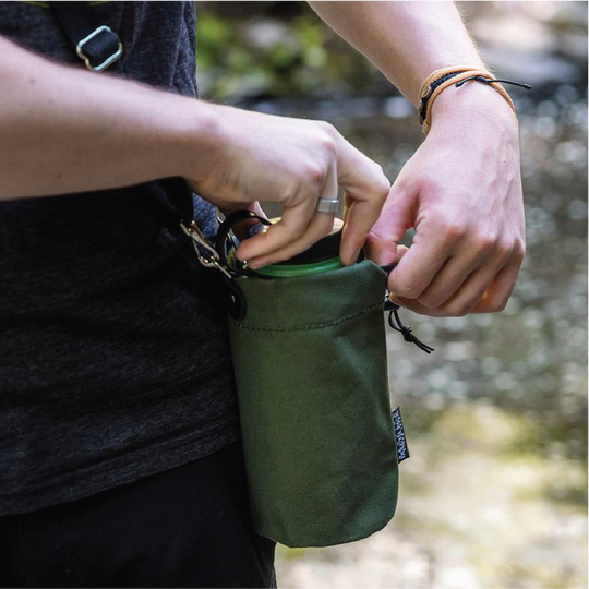 Man putting water bottle into Water Bottle Holder that he is wearing on his hip in the woods
