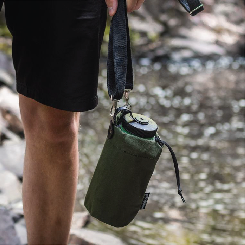 Water Bottle Holder hanging from man's hand in front of creek