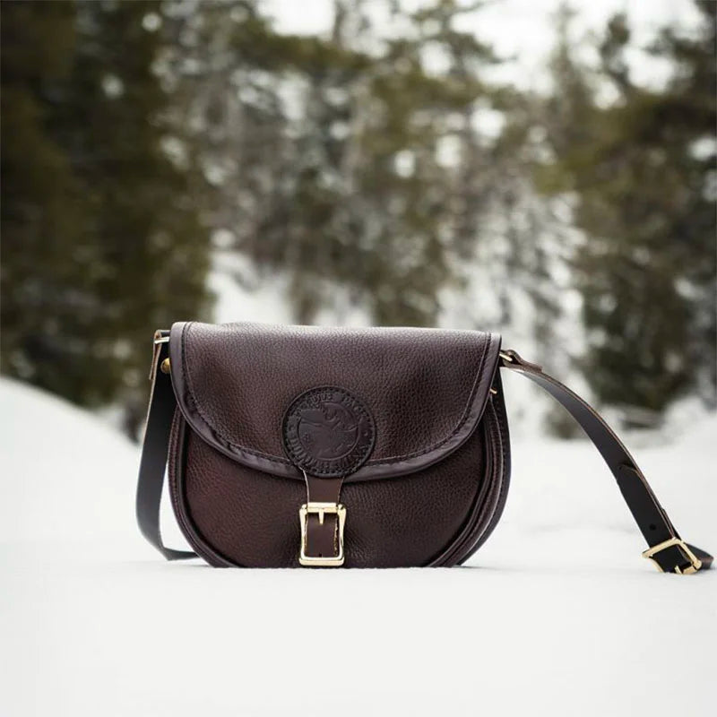 Small Leather Shell Purse in rich brown leather with antique brass buckle, set against a snowy outdoor forest backdrop, showcasing rugged handmade quality.