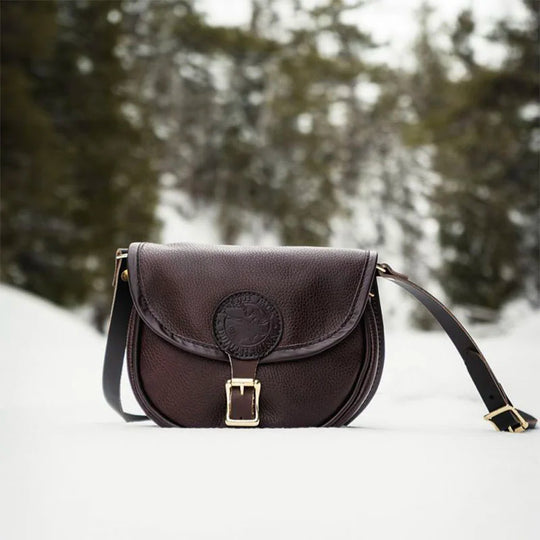 Small Leather Shell Purse in rich brown leather with antique brass buckle, set against a snowy outdoor forest backdrop, showcasing rugged handmade quality.