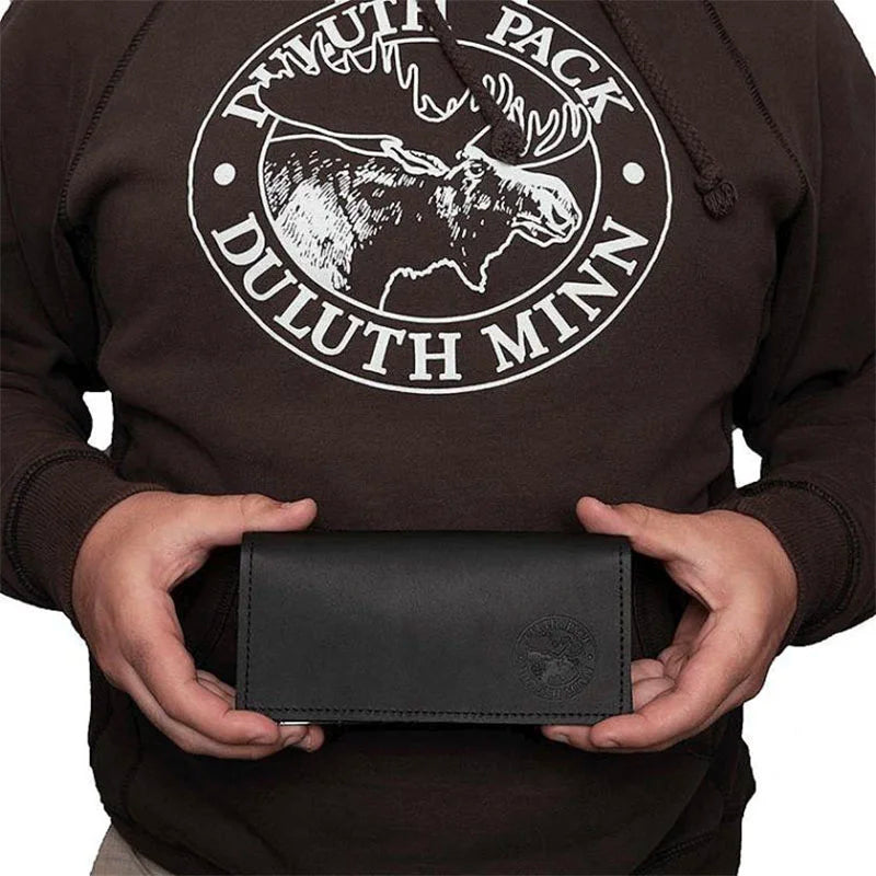 Leather Checkbook Cover in black premium leather with embossed logo, held by person wearing a Duluth Pack hoodie, showcasing durable handmade craftsmanship.