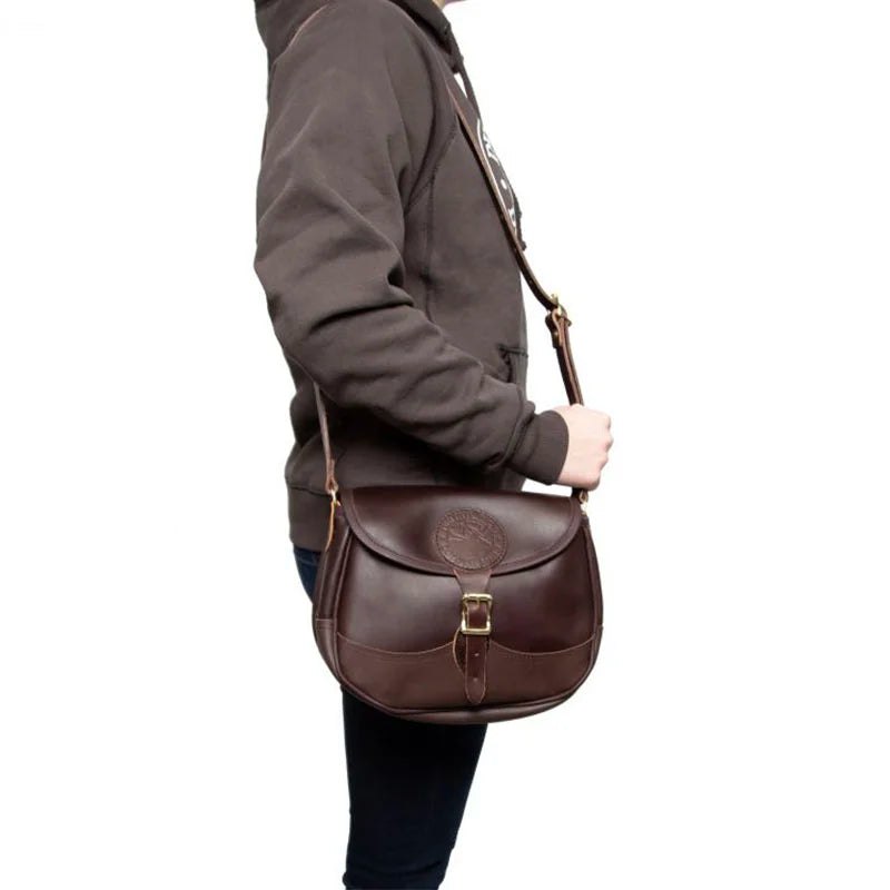 Medium Leather Shell Purse in rich brown premium leather with adjustable strap, worn crossbody by person in casual outdoor attire, crafted by Duluth Pack.